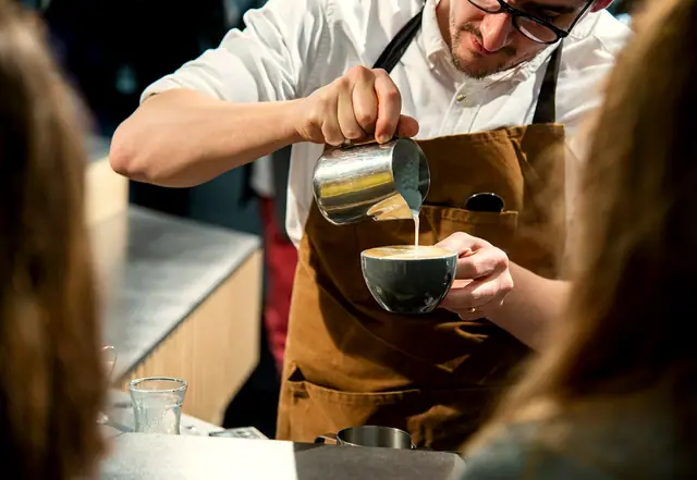 A barista pouring steamed milk into a cup